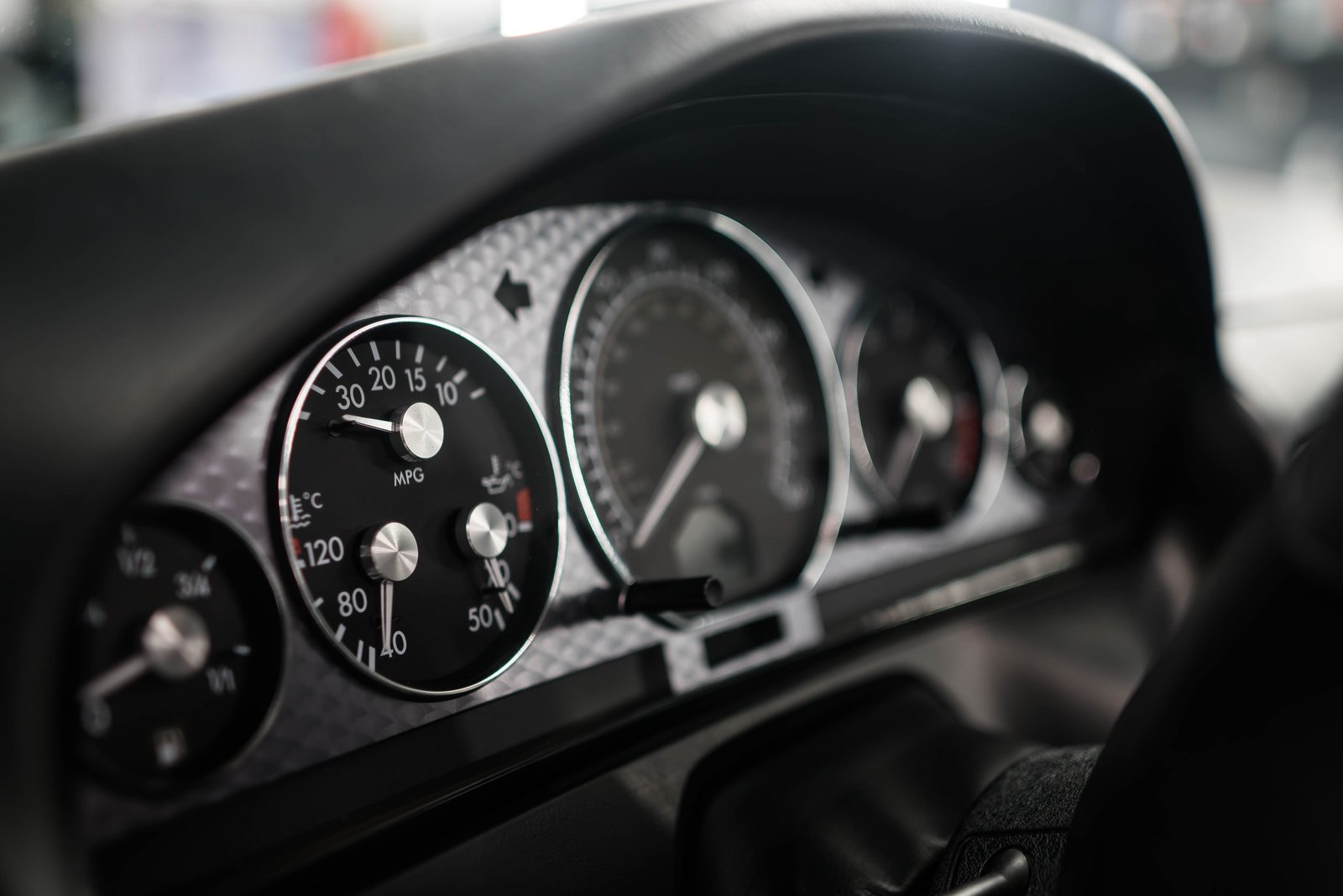 Detailaufnahme des Aston-Martin-Kombiinstruments mit polierten Chrom-Zeigern und Karbonfaser-Zifferblatt — Beispiel für Premium-Innenraumdetailing bei Neowash Braunschweig